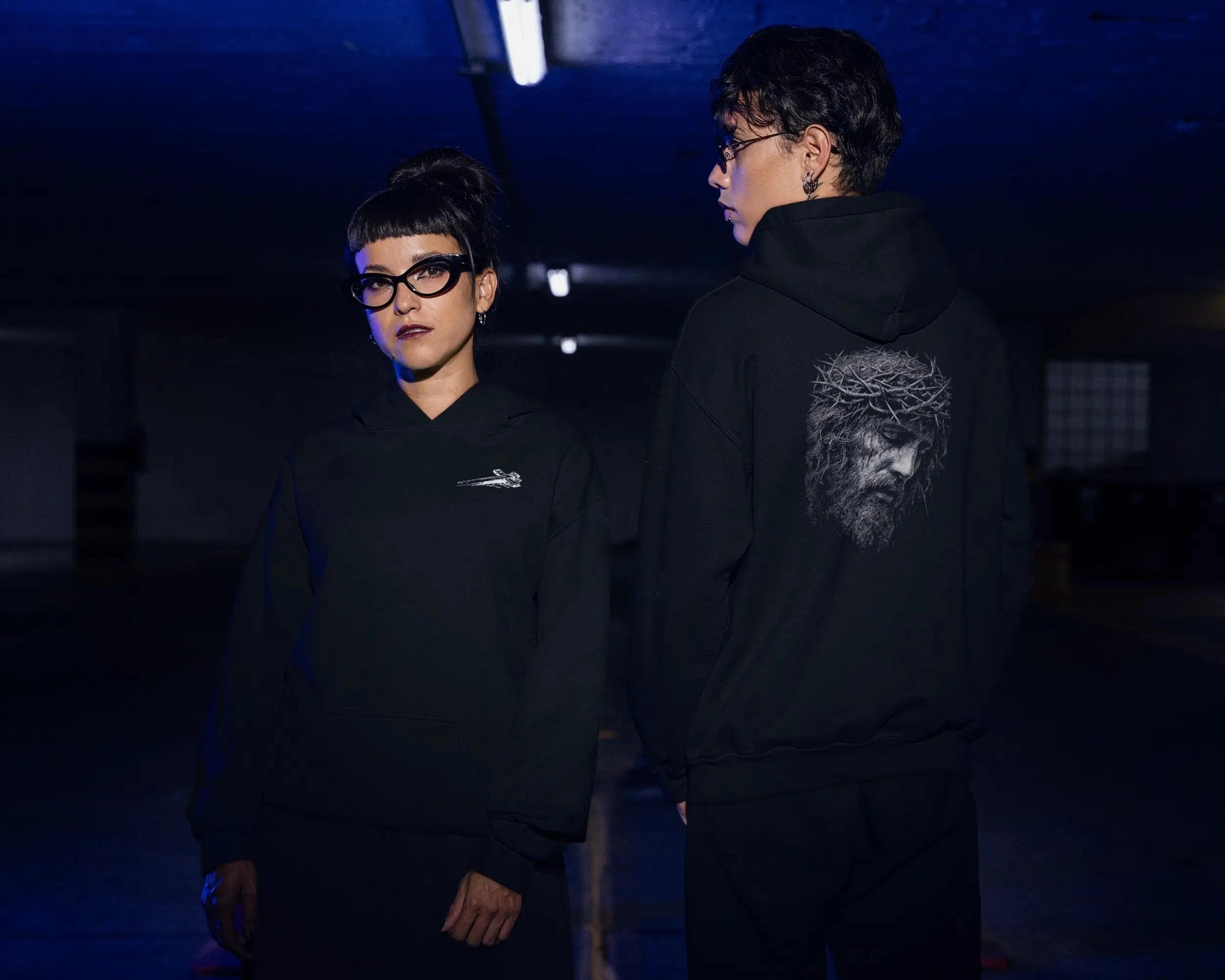 A man and a woman each wearing the Crown of Thorns Hoodie. The woman shows the front graphic and the man is displaying the back graphic.