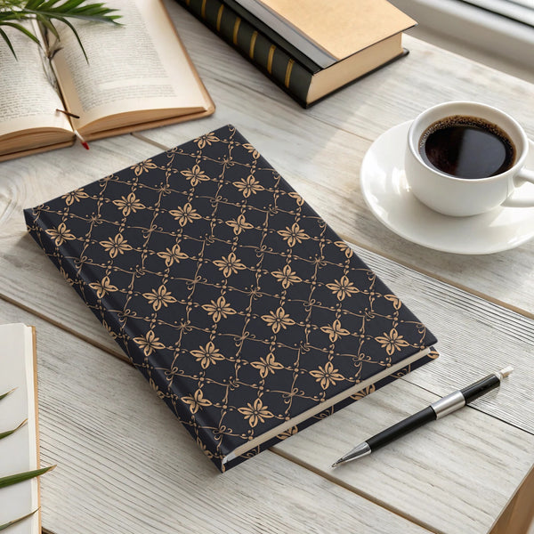 Dark journal with gold floral pattern next to coffee cup and books.