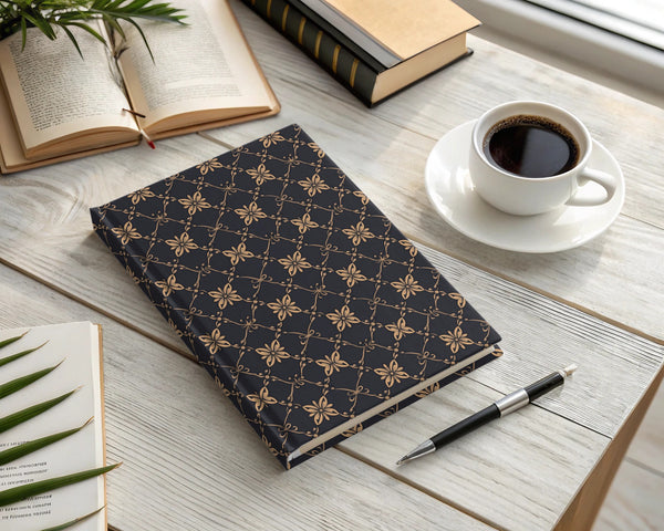 Dark journal with gold floral pattern next to coffee cup and books.