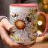 Mug with daisy and bee illustration, held by a person in a grey sweater.