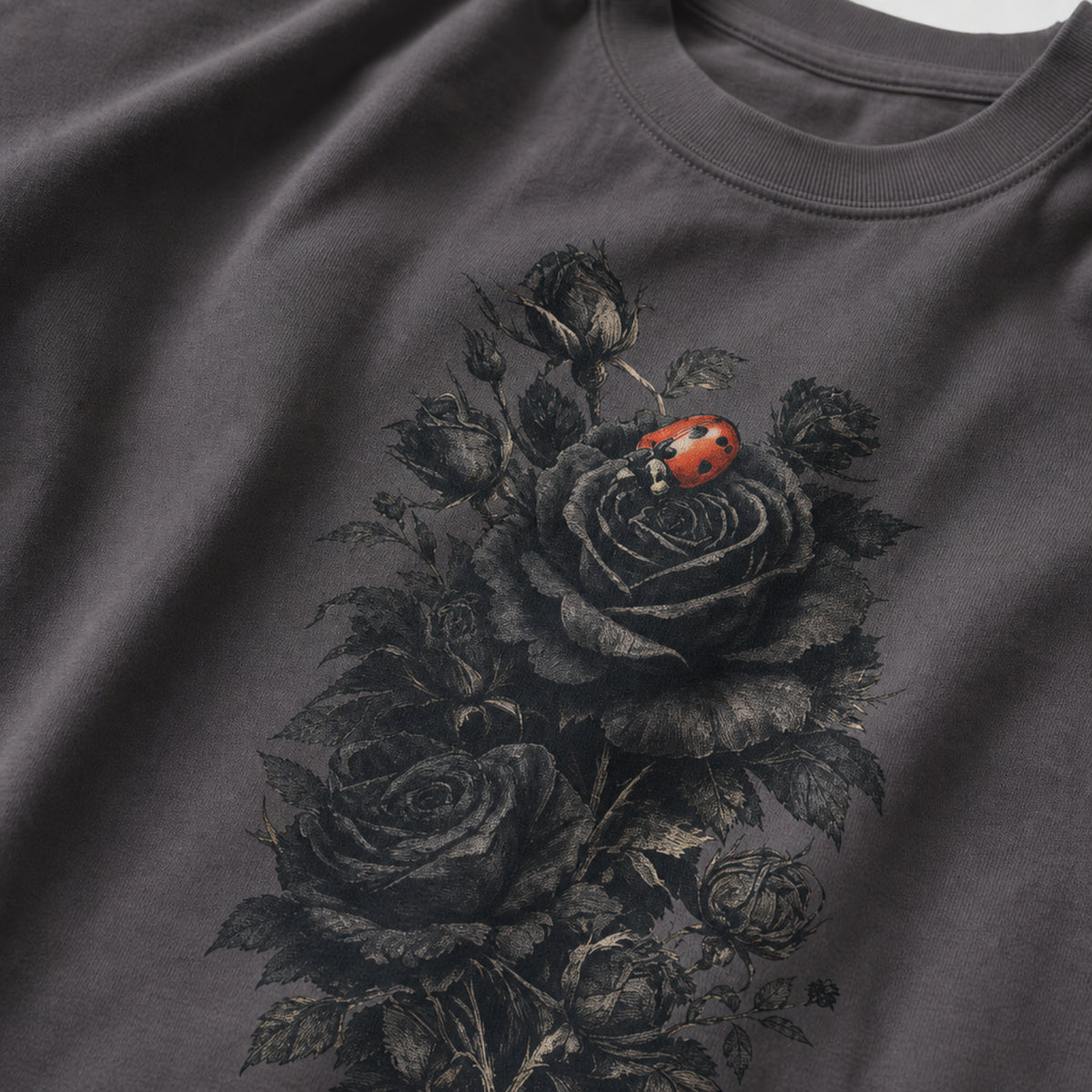 A close-up of a dark gray crewneck t-shirt featuring a detailed graphic print of black roses and a small red ladybug on the front.