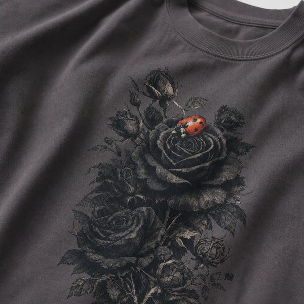 A close-up of a dark gray crewneck t-shirt featuring a detailed graphic print of black roses and a small red ladybug on the front.