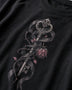 Close-up of a black crewneck t-shirt featuring a detailed graphic print of an ornate key wrapped in a dark ribbon with a pink rose and leaves.