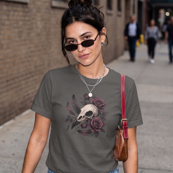 A woman wearing a dark gray graphic t-shirt with a skull and rose design, styled with sunglasses, layered necklaces, and a brown leather shoulder bag, standing on a city sidewalk.