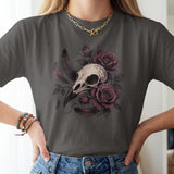 A woman wearing a dark gray t-shirt with a graphic print of a bird skull surrounded by purple roses and feathers, paired with blue jeans.