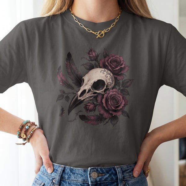 A woman wearing a dark gray t-shirt with a graphic print of a bird skull surrounded by purple roses and feathers, paired with blue jeans.