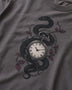 A close-up of a dark gray t-shirt featuring a graphic print of a black snake wrapped around a vintage pocket watch, accented with barbed wire and muted red-purple leaves.