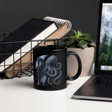 Black mug with octopus design on a desk with laptop, books, and plant