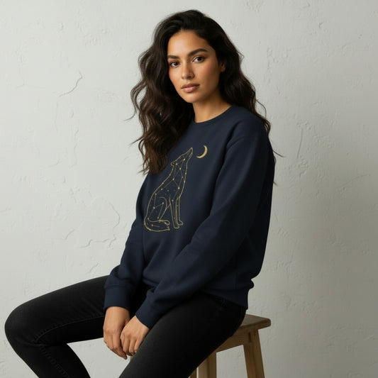 Woman wearing a navy blue sweatshirt with a wolf design sitting on a stool against a light gray wall.