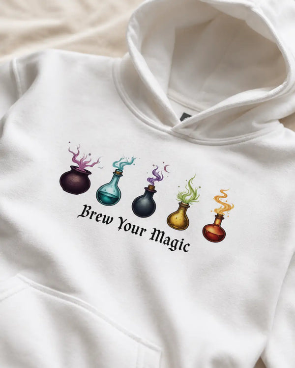 White hoodie with colorful potion bottles and 'Brew Your Magic' text on a beige background XS