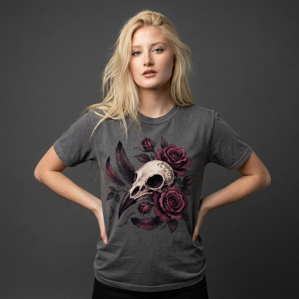 A blonde woman modeling a dark gray t-shirt with a graphic print of a bird skull and dark purple roses, posed against a dark gray studio background.