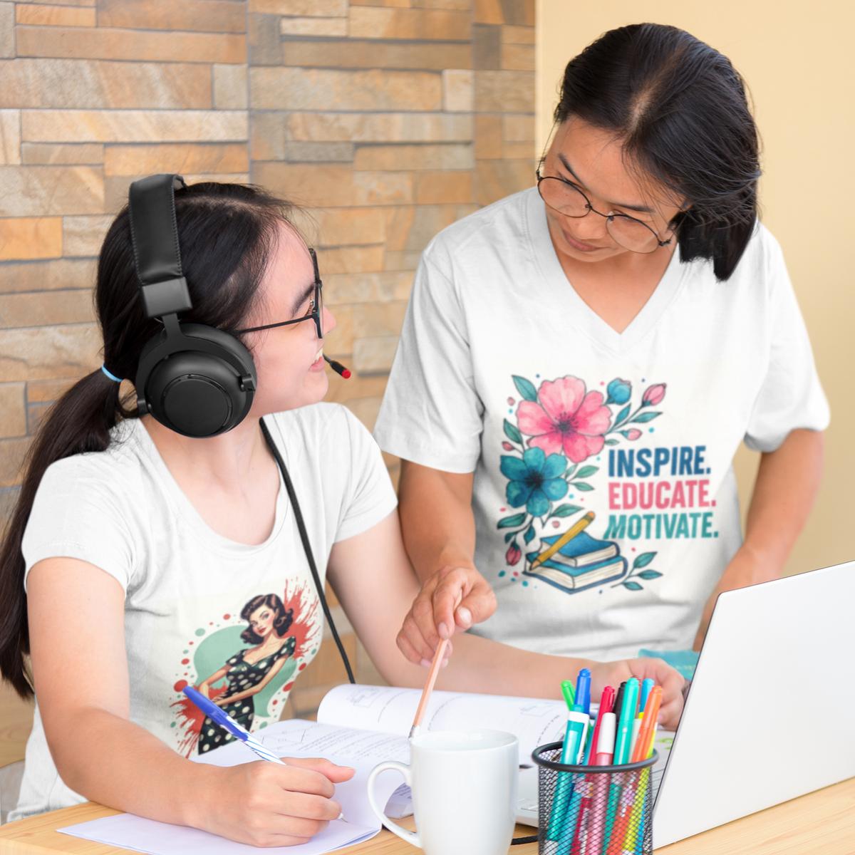 Two people sitting at a table with one wearing headphones and the other holding a pen, both wearing t-shirts with designs.