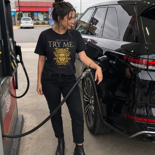Person refueling a black SUV at a gas station wearing a black t-shirt with text and graphics. 