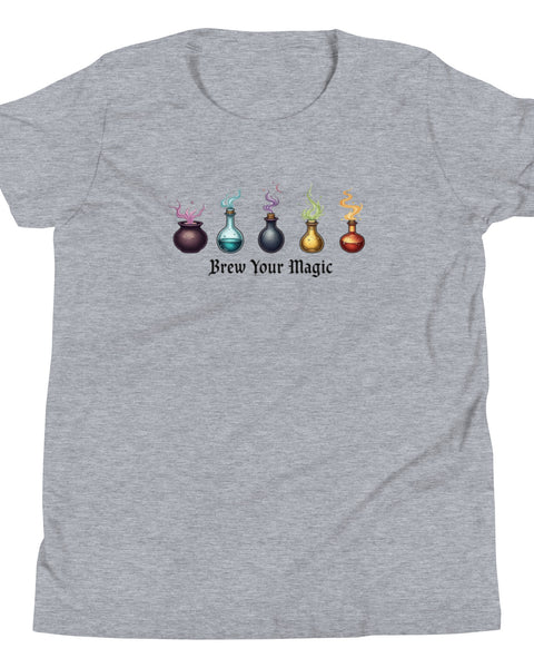 A grey youth staple t-shirt displaying a graphic of five different colored potion bottles, each emitting a wisp of colored smoke. Below the bottles, the text "Brew Your Magic" is written in a dark, stylized font.