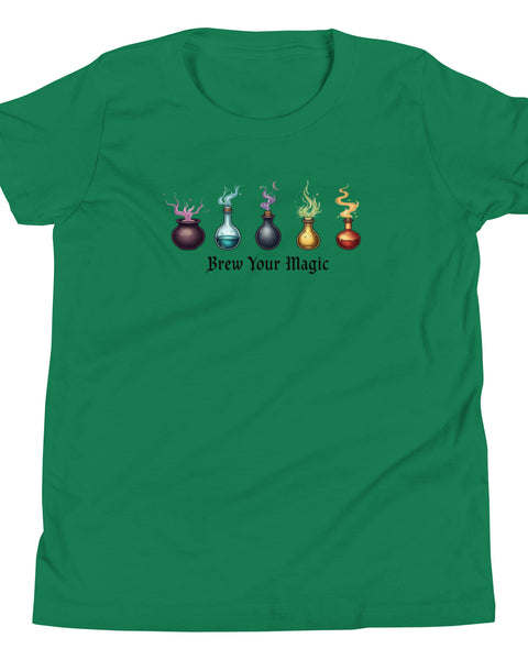 A green youth staple t-shirt displaying a graphic of five different colored potion bottles, each emitting a wisp of colored smoke. Below the bottles, the text "Brew Your Magic" is written in a dark, stylized font.