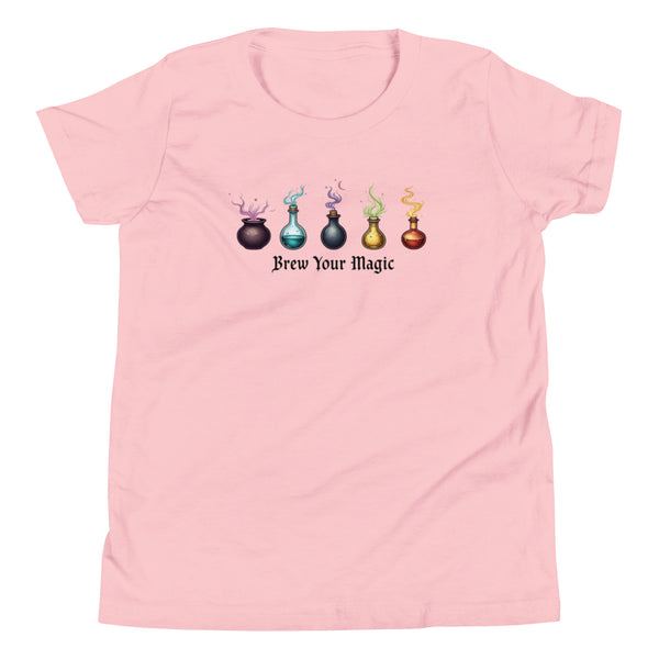 A pink youth staple t-shirt displaying a graphic of five different colored potion bottles, each emitting a wisp of colored smoke. Below the bottles, the text "Brew Your Magic" is written in a dark, stylized font.