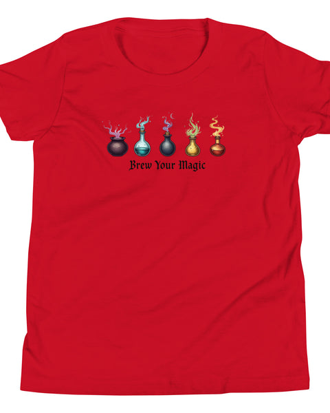 A red youth staple t-shirt displaying a graphic of five different colored potion bottles, each emitting a wisp of colored smoke. Below the bottles, the text "Brew Your Magic" is written in a dark, stylized font.